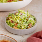 A small bowl of shaved brussels sprouts caesar salad piled high. More salad in the background.