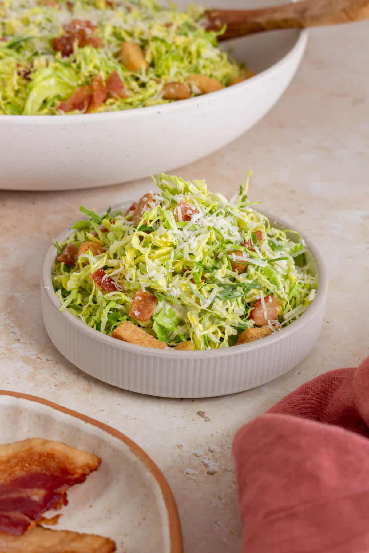 A small bowl of shaved brussels sprouts caesar salad piled high. More salad in the background.
