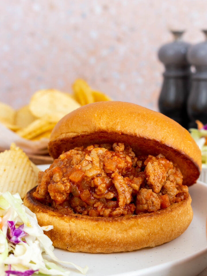 A plate with turkey sloppy joes on a broiche bun. Coleslaw and chips on the side.