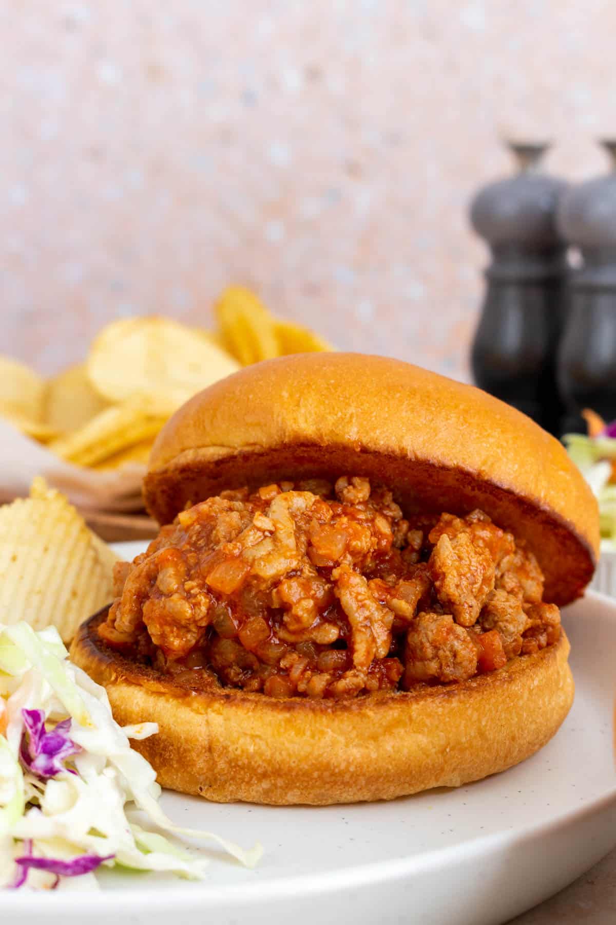 A plate with turkey sloppy joes on a broiche bun. Coleslaw and chips on the side.