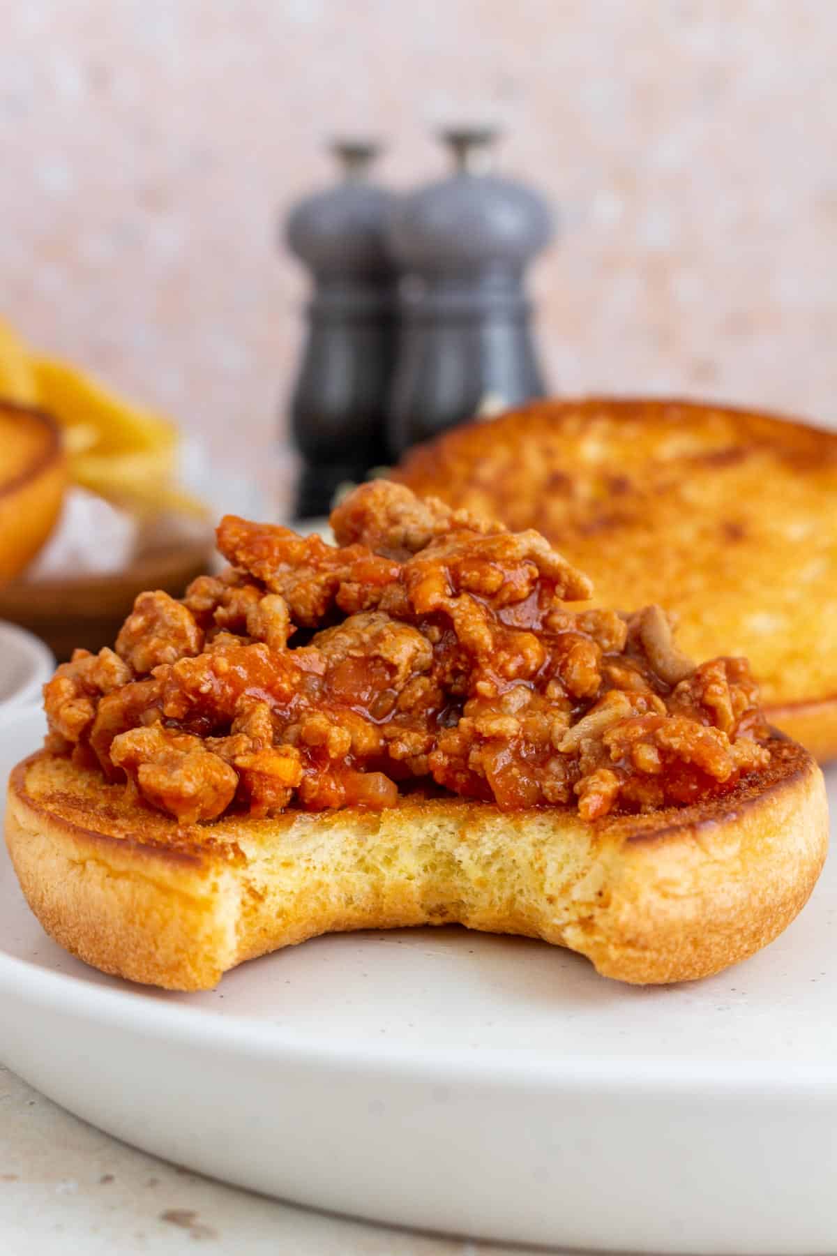 A scoop of turkey sloppy joes piled on top of the bottom of a toasted bun with a bite taken out.