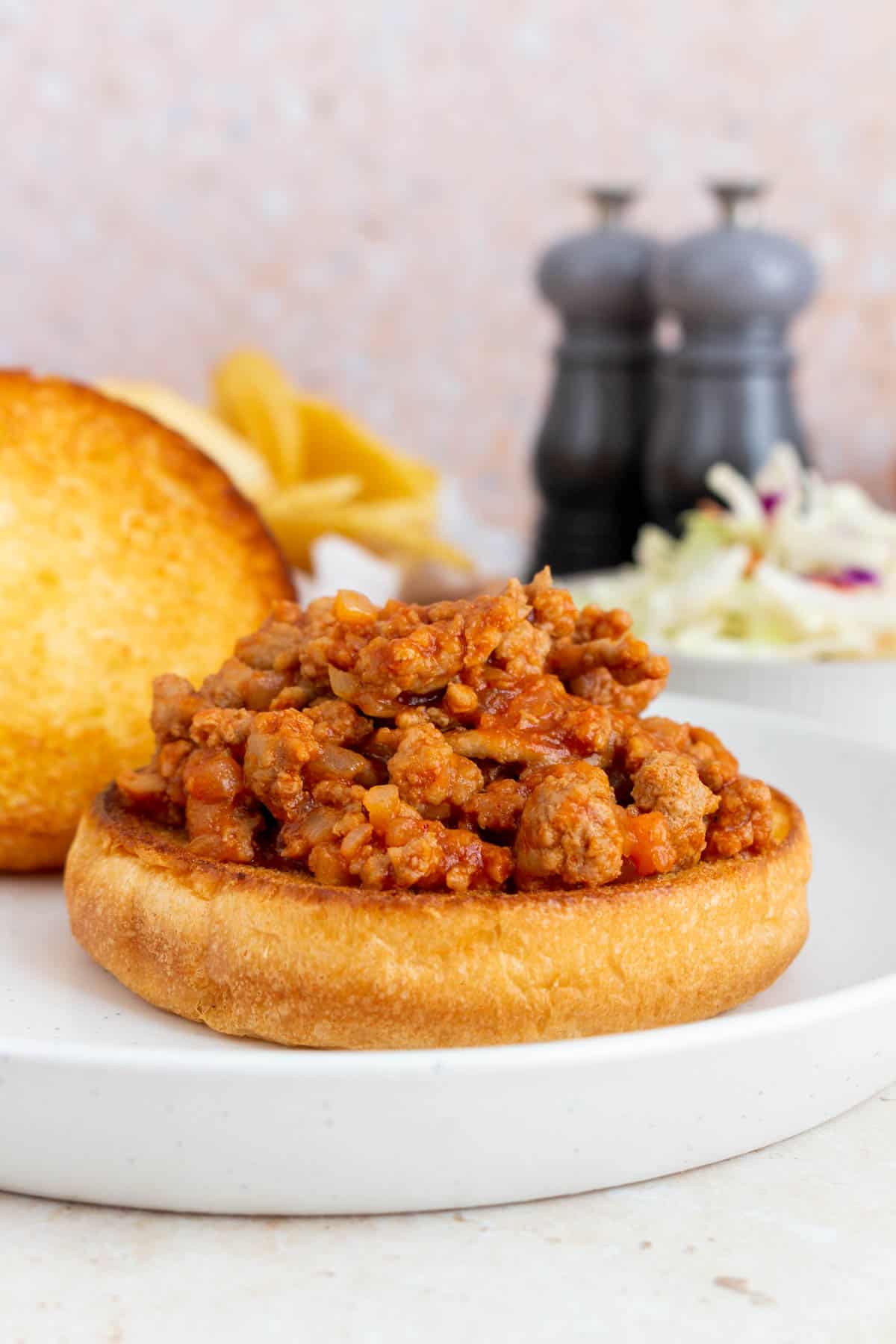 A white plate with turkey sloppy joes on a burger bun. Salt and pepper shakers in the background.