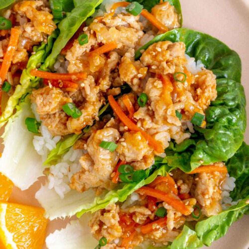 Overhead view of four spicy orange chicken lettuce wraps on a plate.