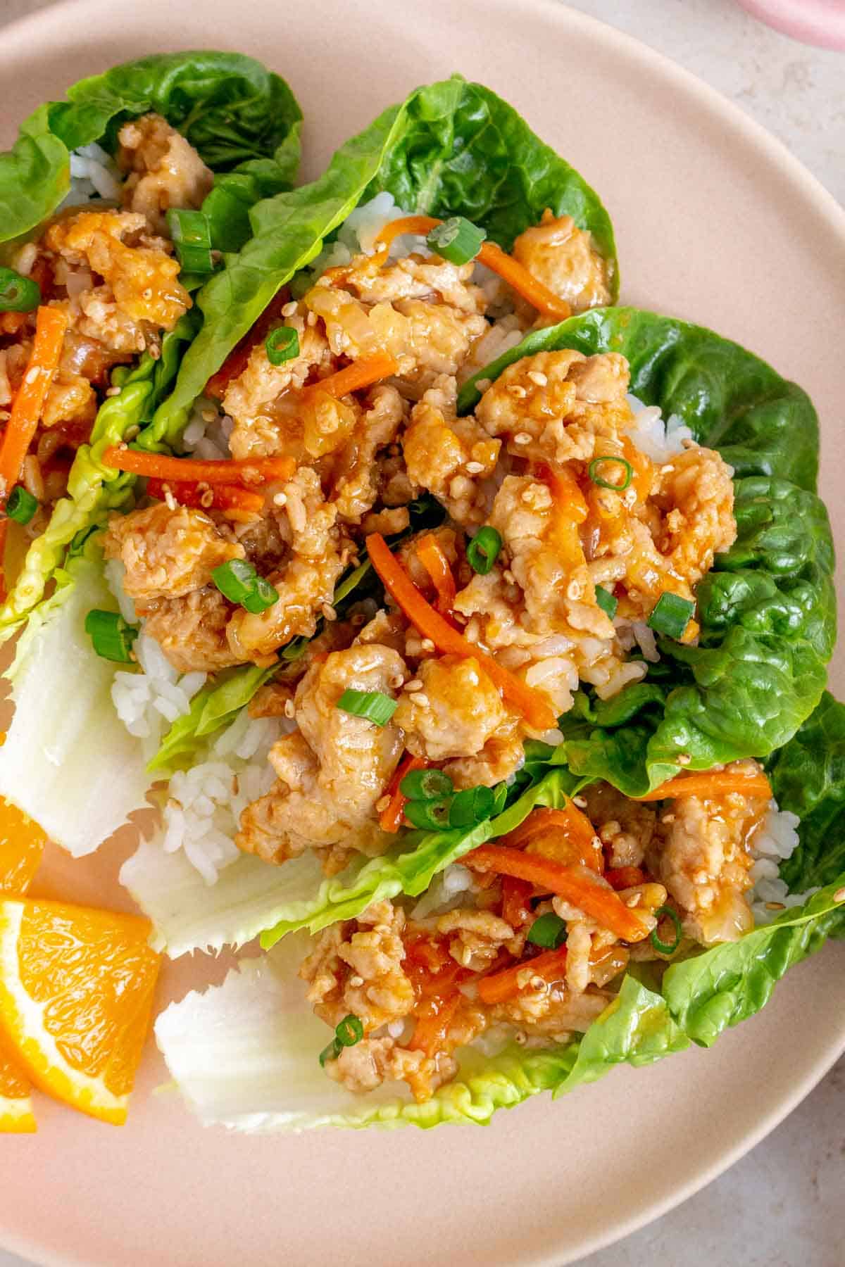 Overhead view of four spicy orange chicken lettuce wraps on a plate.
