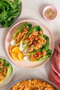 Overhead view of a plate with four spicy orange chicken lettuce wraps along with orange slices.
