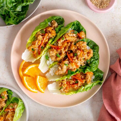 Overhead view of a plate with four spicy orange chicken lettuce wraps along with orange slices.