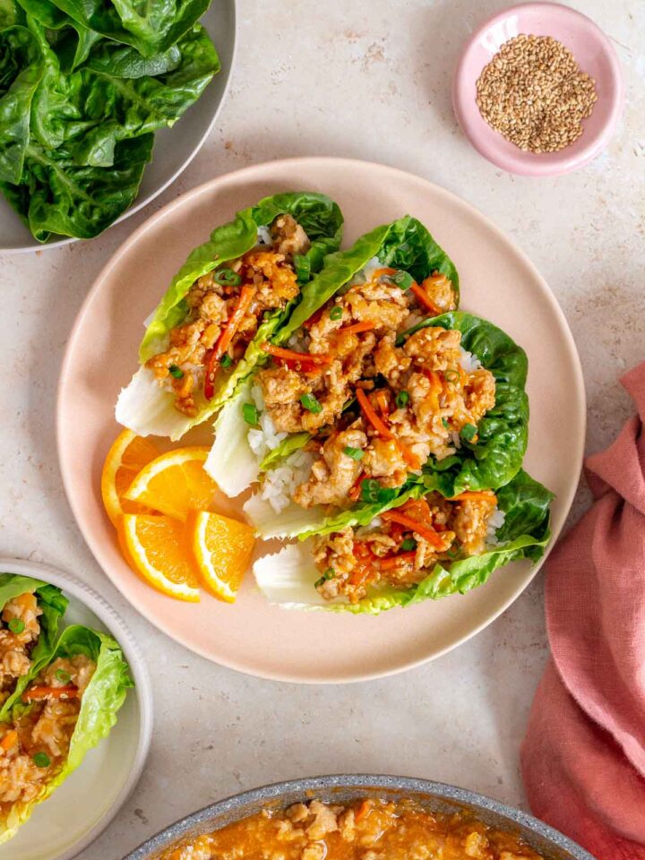 Overhead view of a plate with four spicy orange chicken lettuce wraps along with orange slices.