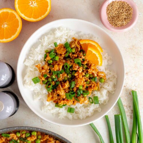 A volcano chicken bowl with rice topped with green onions and sesame seeds and orange slices.