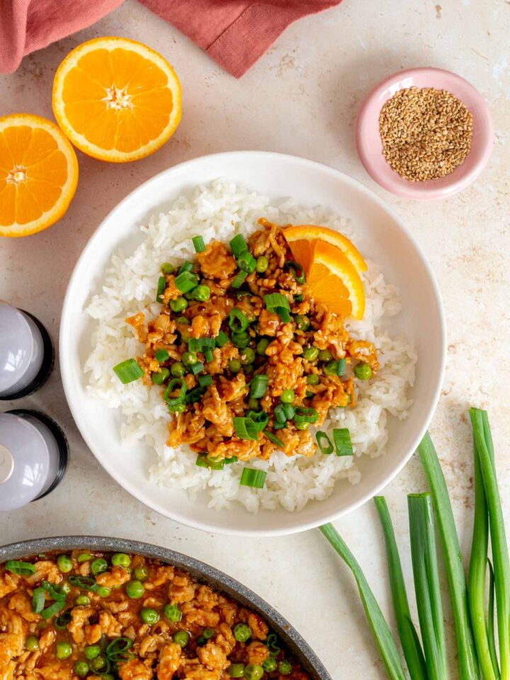 A volcano chicken bowl with rice topped with green onions and sesame seeds and orange slices.