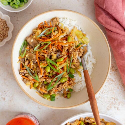 A bowl of egg roll in a bowl with ground turkey and extra veggies over rice with a fork.