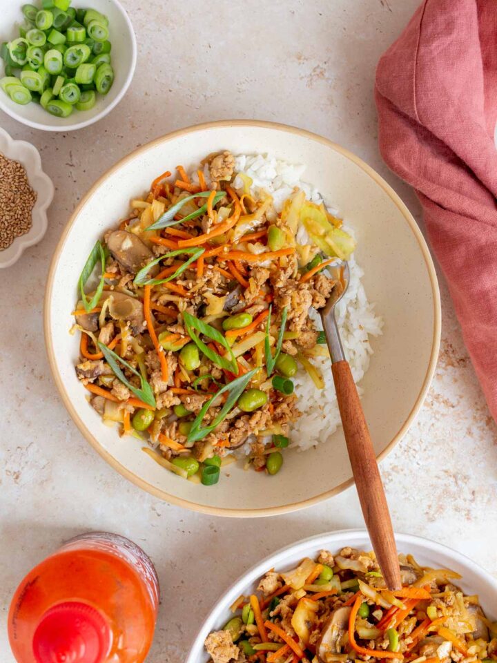 A bowl of egg roll in a bowl with ground turkey and extra veggies over rice with a fork.