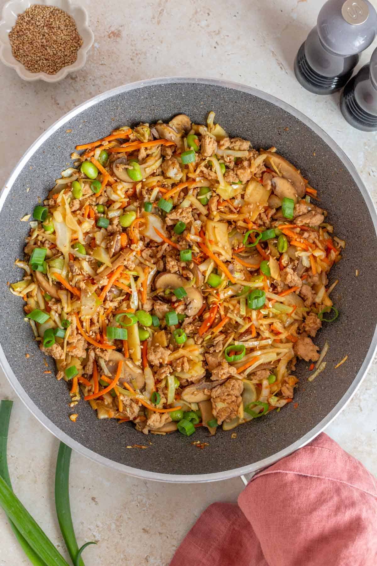 An overhead view of a skillet of egg roll in a bowl with ground turkey and extra veggies topped with green onions and sesame seeds.