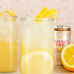 A glass of pear ginger mocktail with a lemon twist garnish. A can of Canada Dry ginger in the back with lemons.
