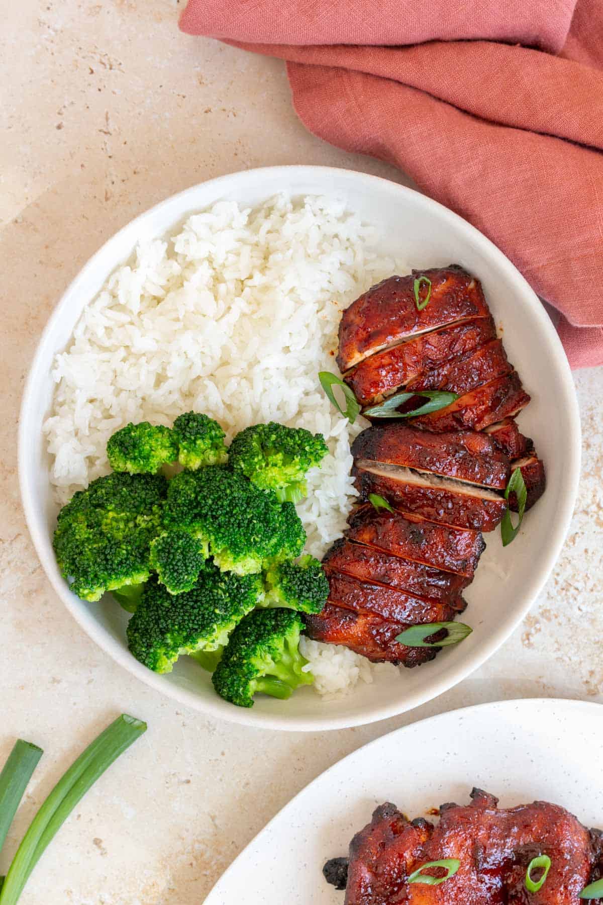 A plate of rice and broccoli with sliced char siu chicken topped with green onions.