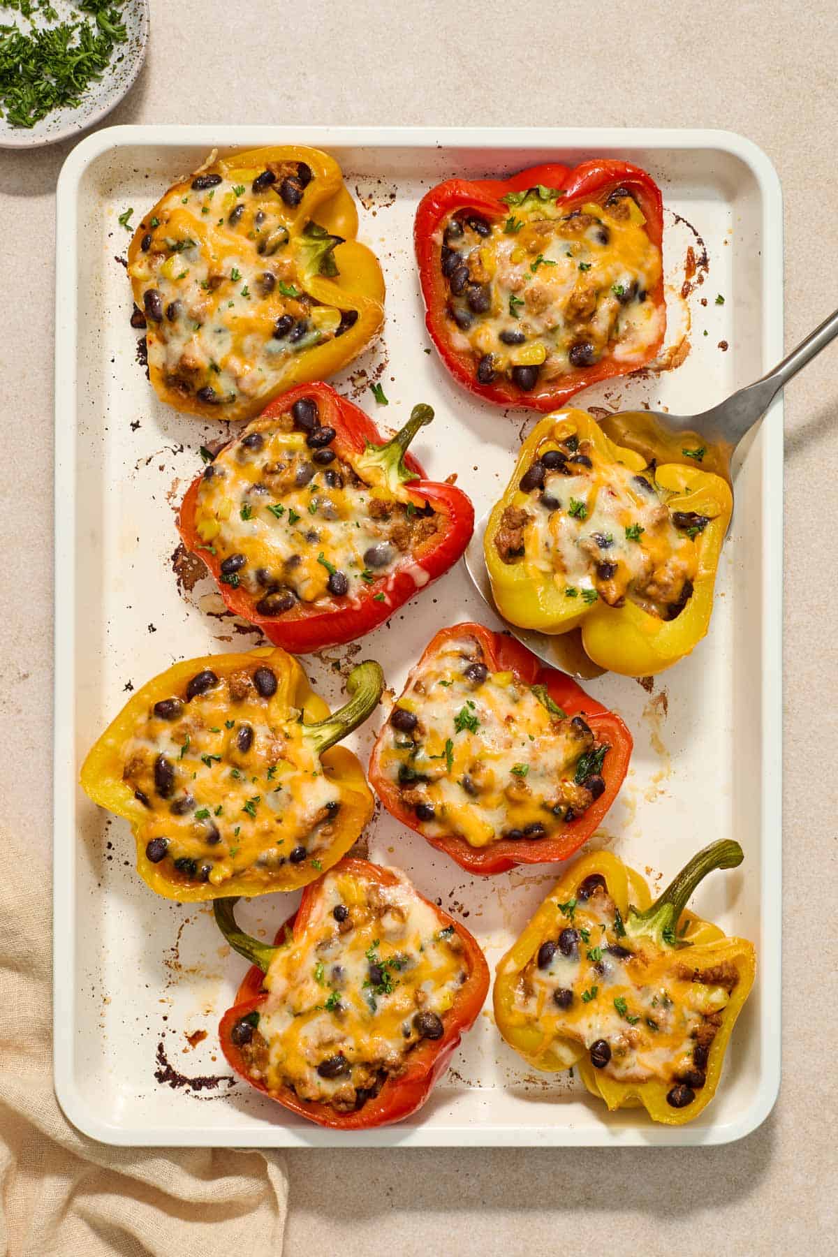 A sheet pan with taco stuffed peppers with extra veggies with a spatula underneath one pepper.
