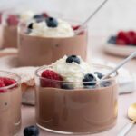 A profile view of jars of cottage cheese chocolate mousse topped with whipped cream and berries.