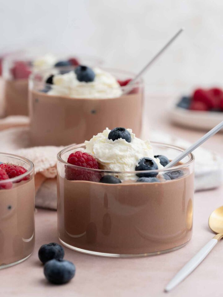 A profile view of jars of cottage cheese chocolate mousse topped with whipped cream and berries.