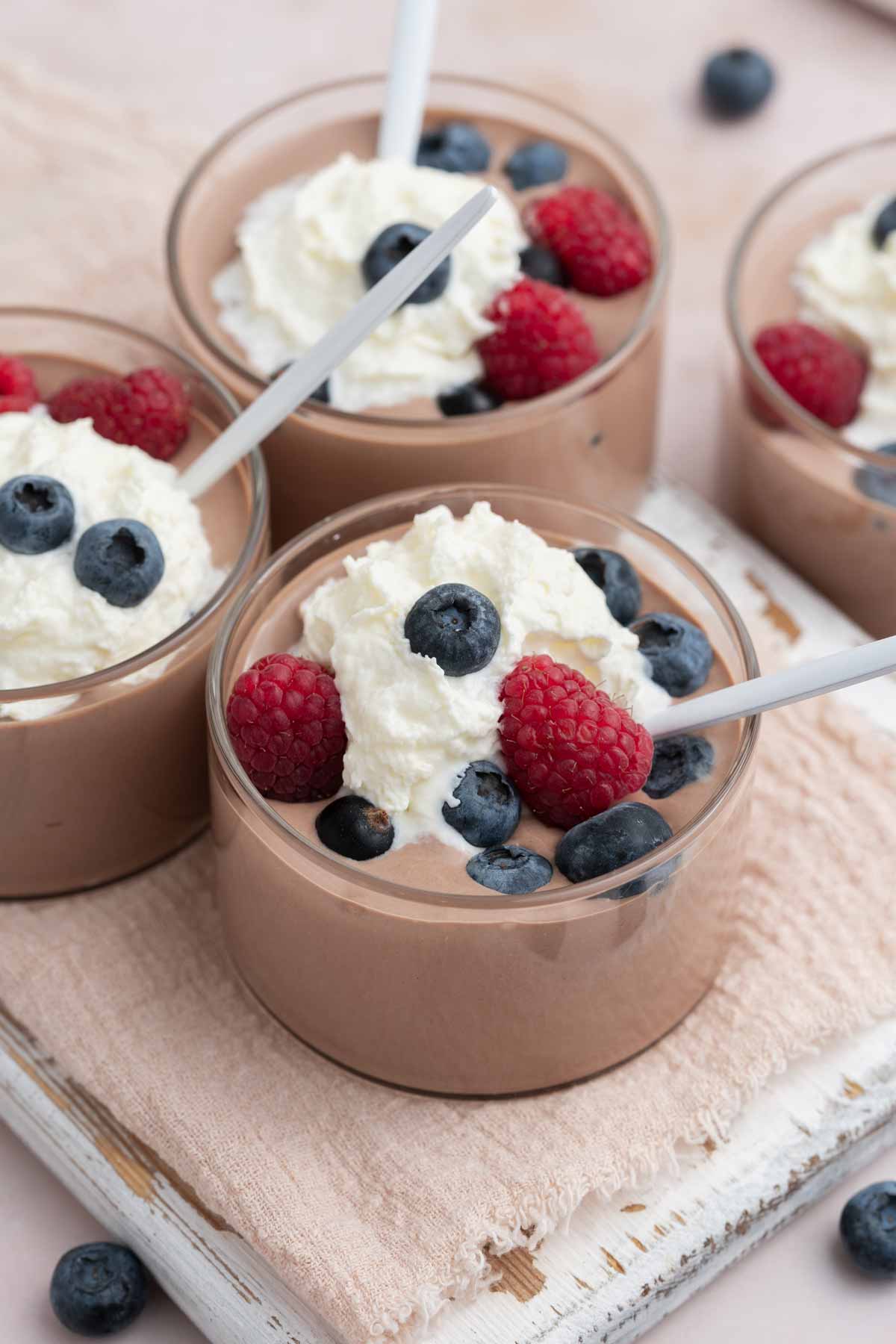 Three jars of cottage cheese chocolate mousse with spoons inside, topped with whipped cream and fresh berries.