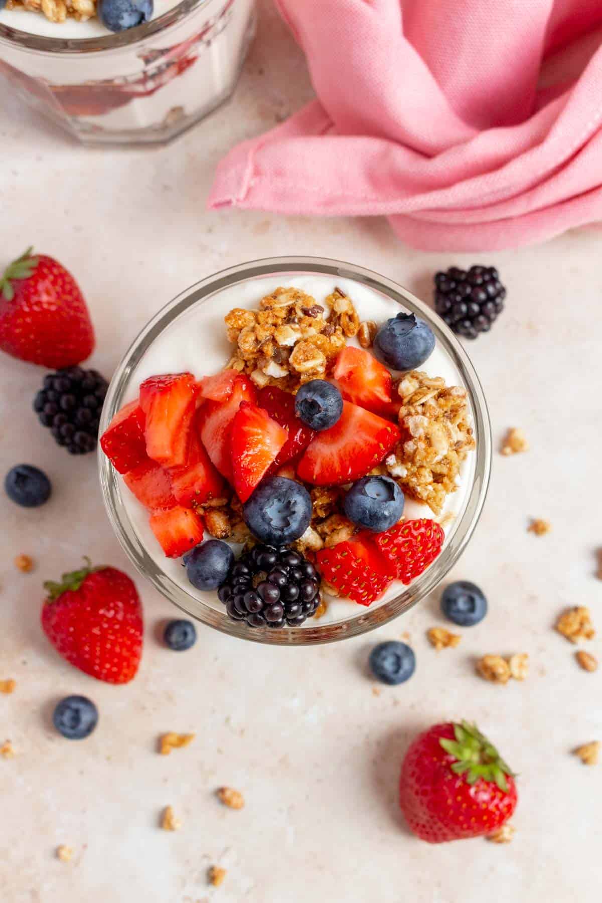 Overhead view of a jar of cottage cheese parfait showing the granola and assorted berries on top. More berries and granola scattered around.