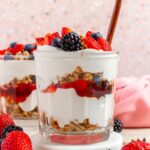A profile view glass of cottage cheese parfait showing the layers with a spoon inserted. Berries on top.