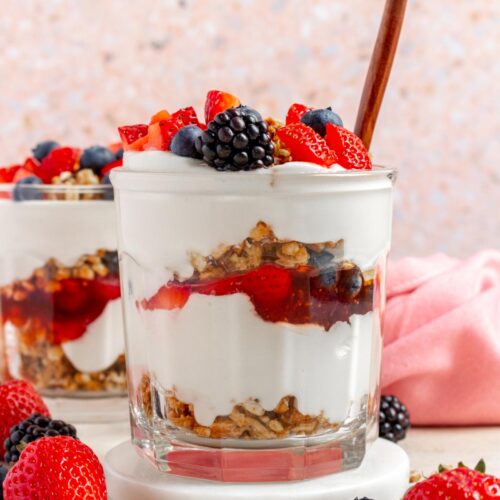 A profile view glass of cottage cheese parfait showing the layers with a spoon inserted. Berries on top.