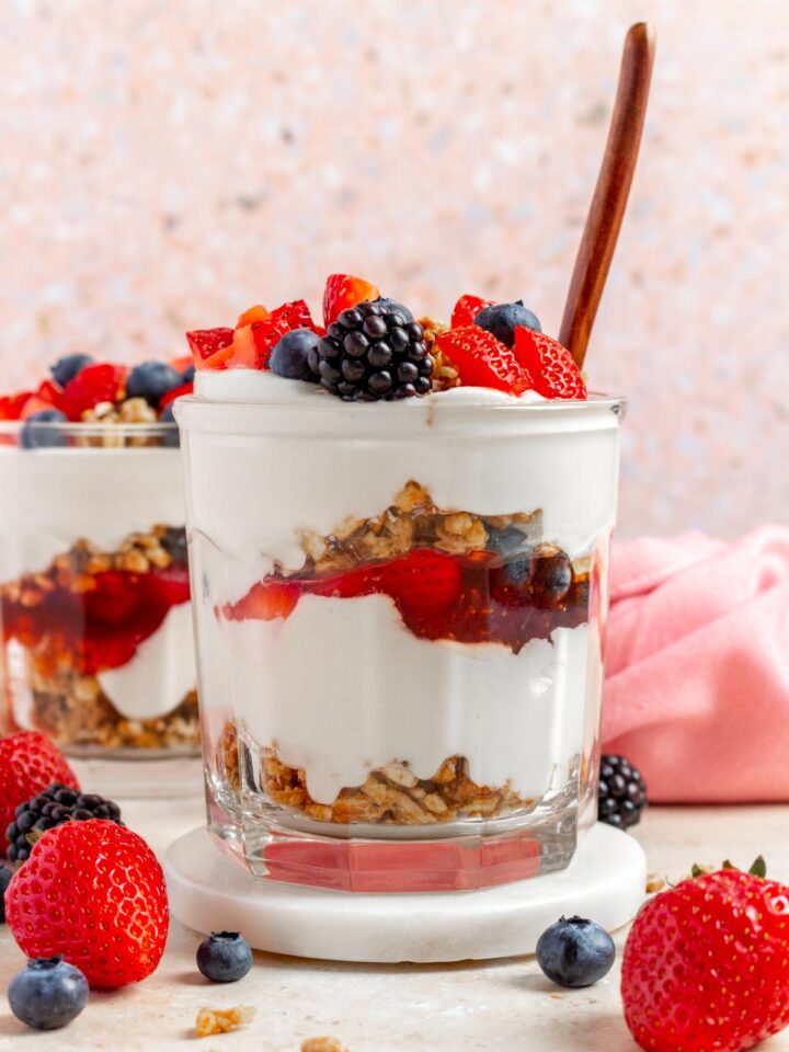 A profile view glass of cottage cheese parfait showing the layers with a spoon inserted. Berries on top.