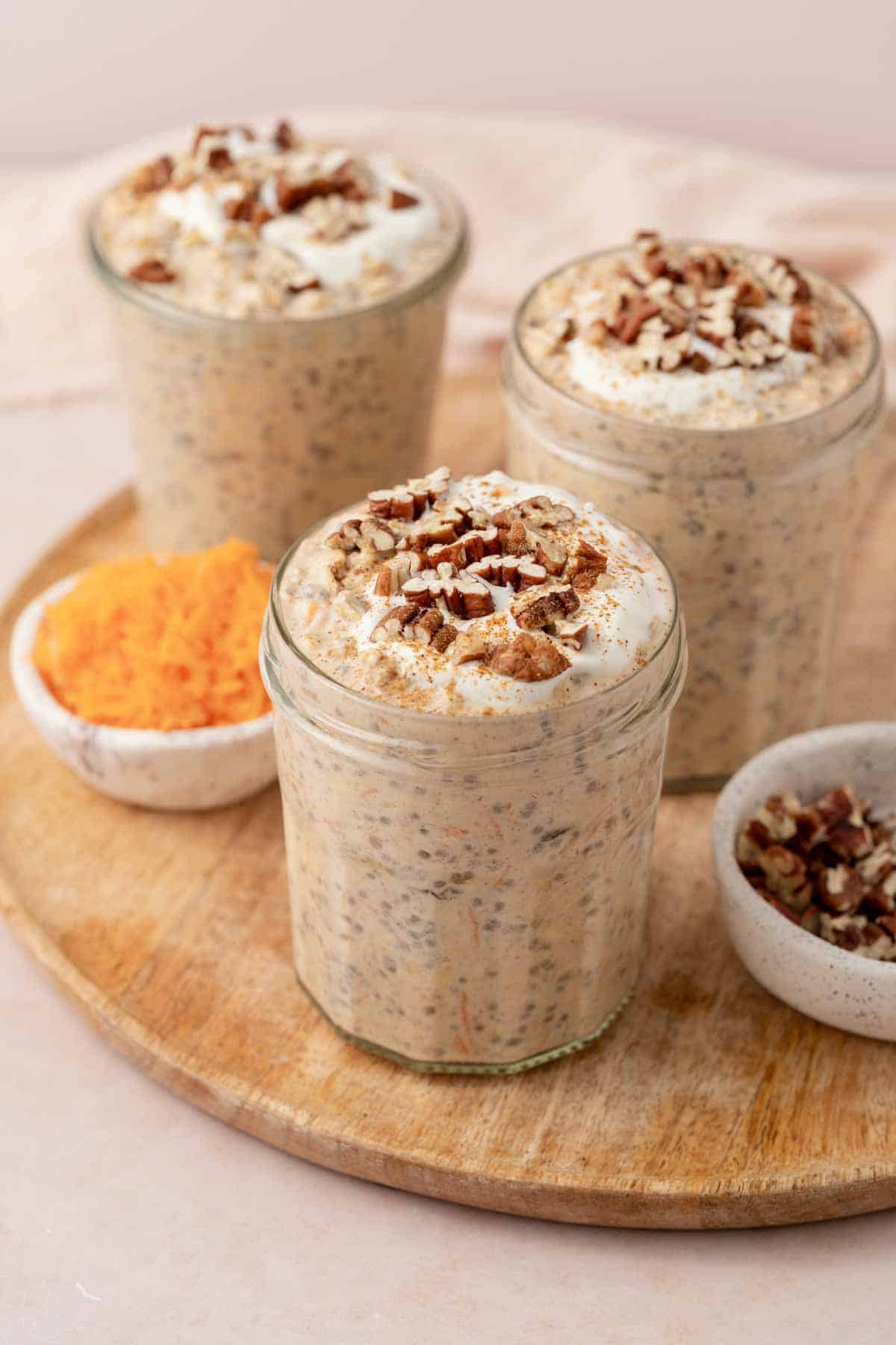 Jars of carrot cake overnight oats topped with Greek yogurt and chopped pecans.
