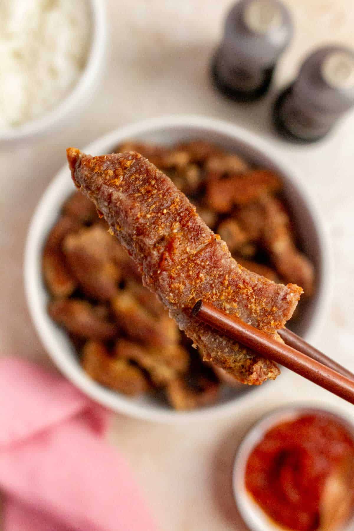 A chopstick holding up a piece of air fryer salt and pepper pork bite.