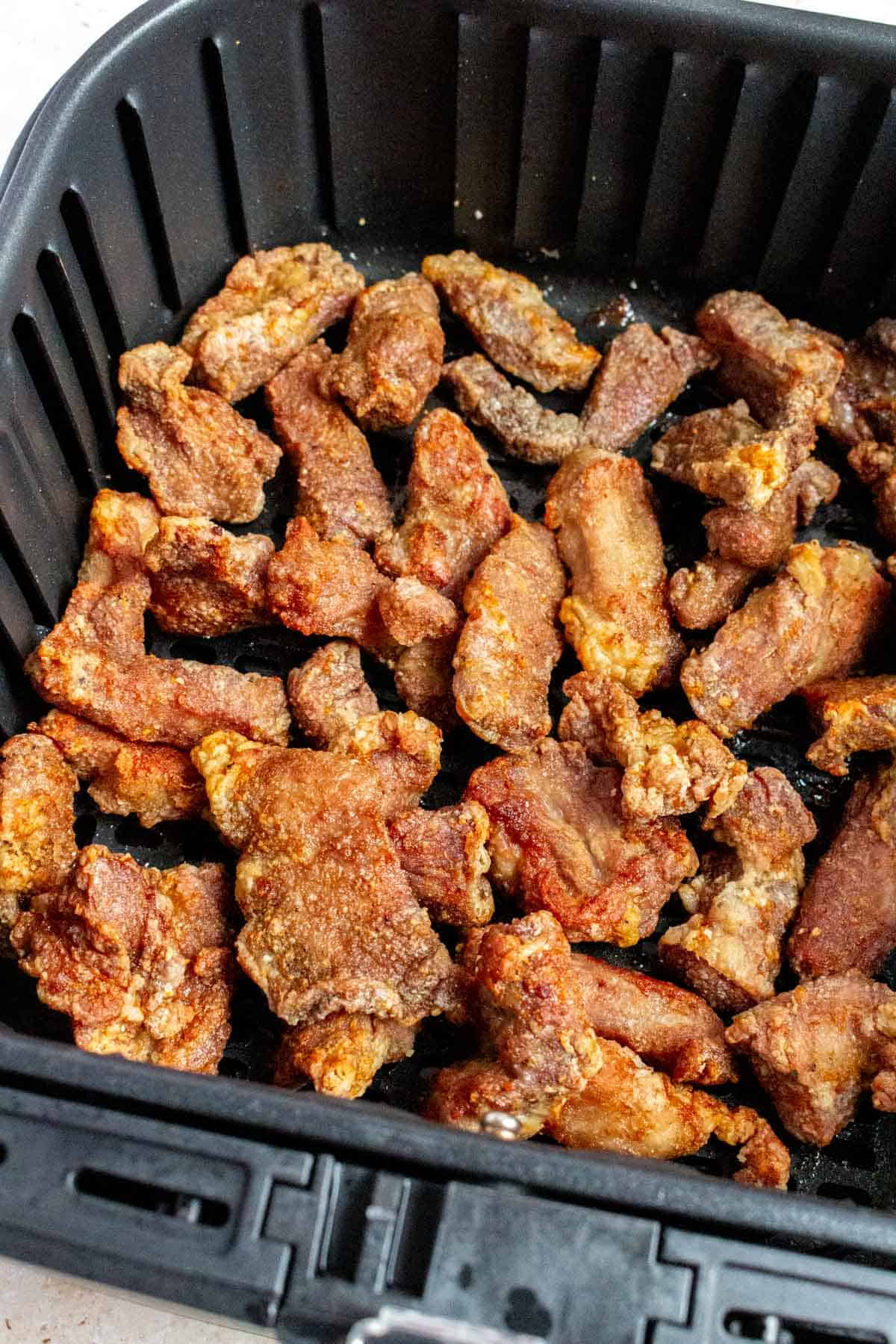Salt and pepper pork bites in an air fryer basket.