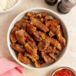 Overhead view of air fryer salt and pepper pork bites in a platter. Salt and pepper shake on the side with some dipping sauce and a bowl of rice.