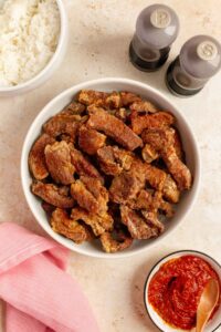 Overhead view of air fryer salt and pepper pork bites in a platter. Salt and pepper shake on the side with some dipping sauce and a bowl of rice.