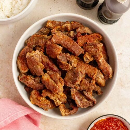Overhead view of air fryer salt and pepper pork bites in a platter. Salt and pepper shake on the side with some dipping sauce and a bowl of rice.