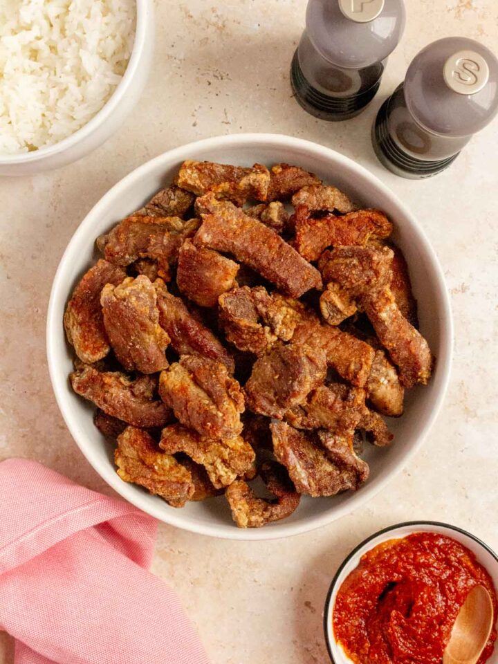 Overhead view of air fryer salt and pepper pork bites in a platter. Salt and pepper shake on the side with some dipping sauce and a bowl of rice.