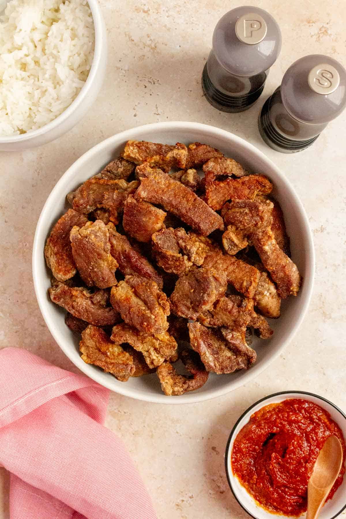 Overhead view of air fryer salt and pepper pork bites in a platter. Salt and pepper shake on the side with some dipping sauce and a bowl of rice.
