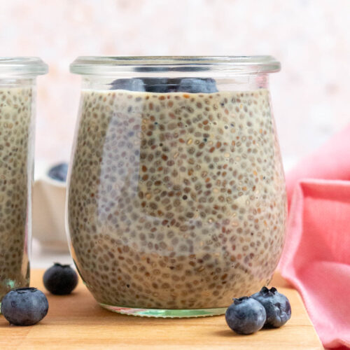 A profile view of a jar of earl grey chia pudding topped with blueberries. More blueberries scattered around.