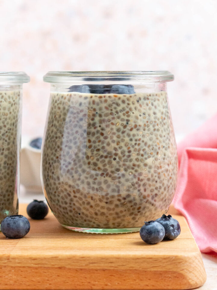 A profile view of a jar of earl grey chia pudding topped with blueberries. More blueberries scattered around.