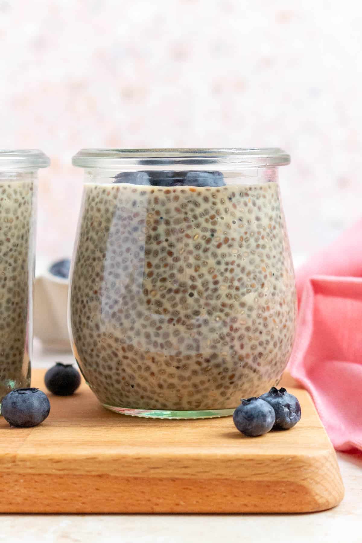 A profile view of a jar of earl grey chia pudding topped with blueberries. More blueberries scattered around.
