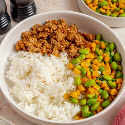 A close up view of hot honey ground pork bowl with corn and edamame topped with roasted sesame seeds.