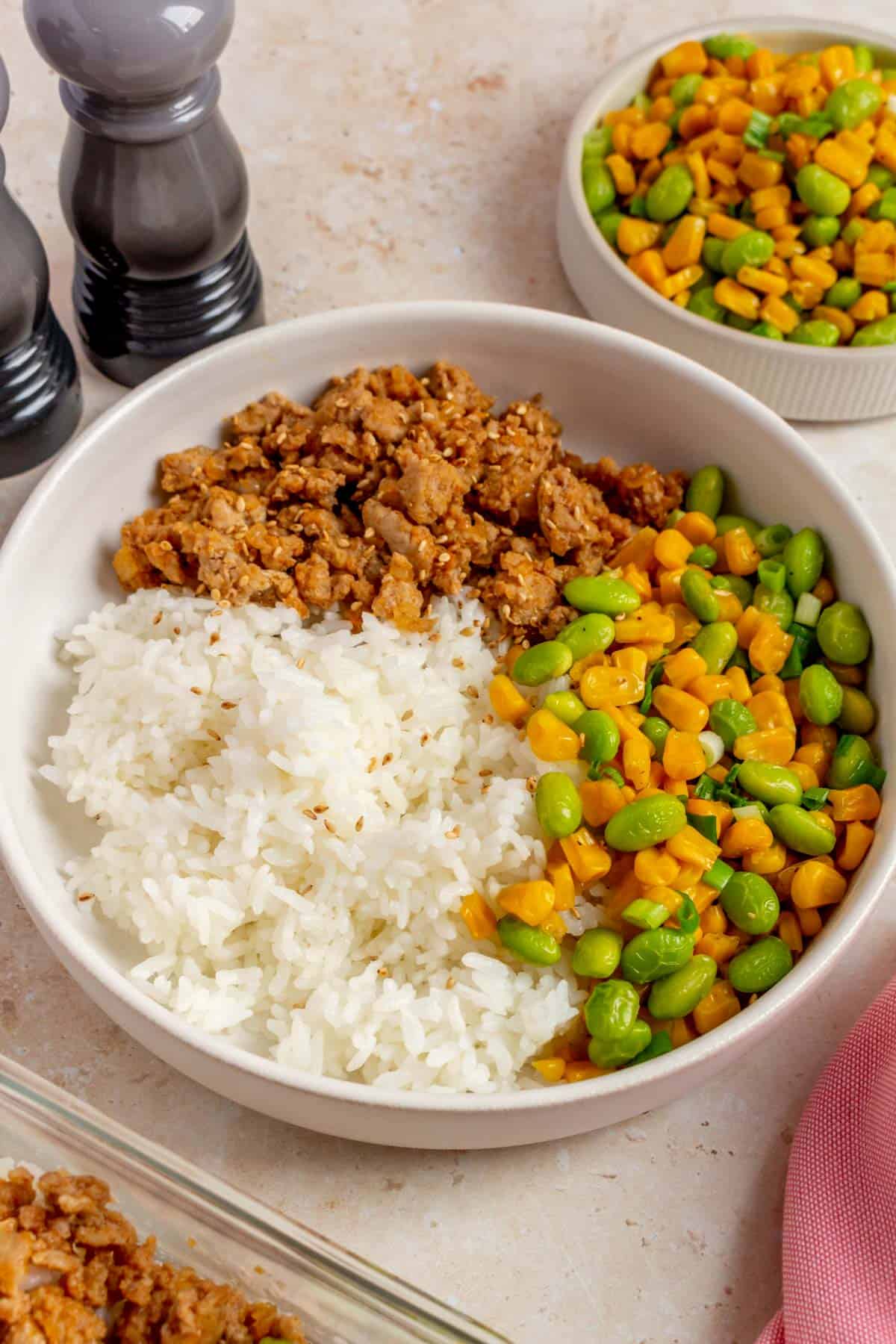 A close up view of hot honey ground pork bowl with corn and edamame topped with roasted sesame seeds.