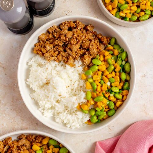 An overhead view of a hot honey ground pork bowl with corn and edamame. Salt and pepper on the side along with another bowl and a plate of just corn and edamame.