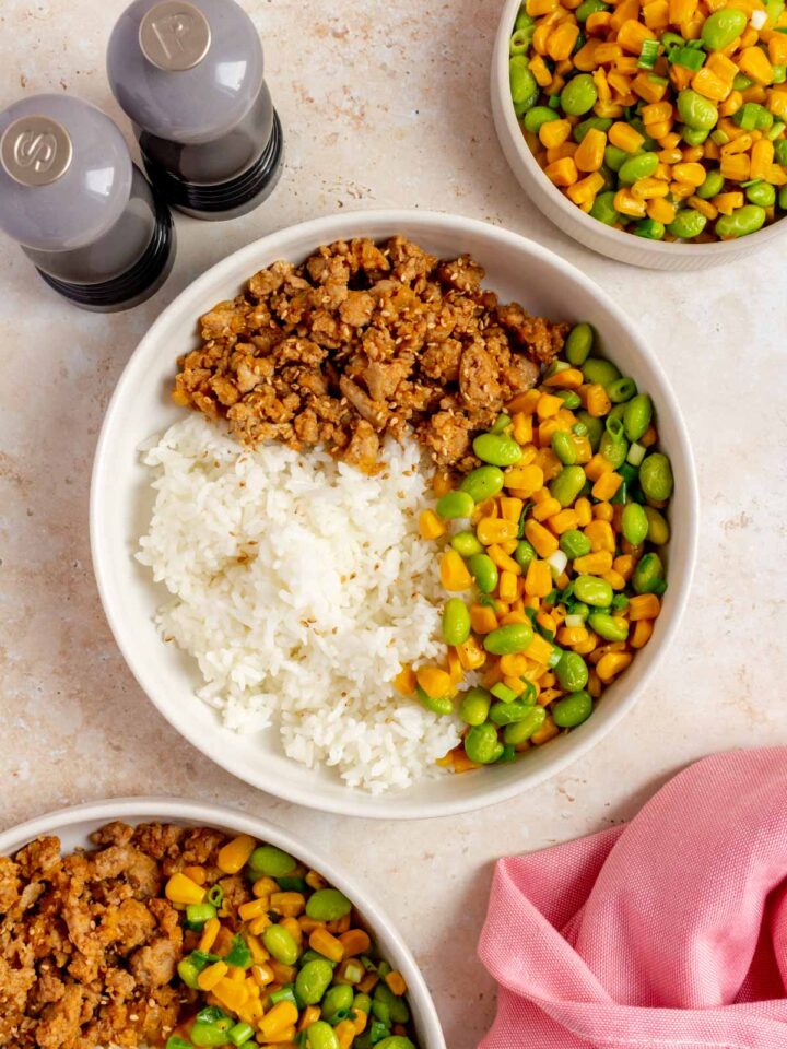 An overhead view of a hot honey ground pork bowl with corn and edamame. Salt and pepper on the side along with another bowl and a plate of just corn and edamame.