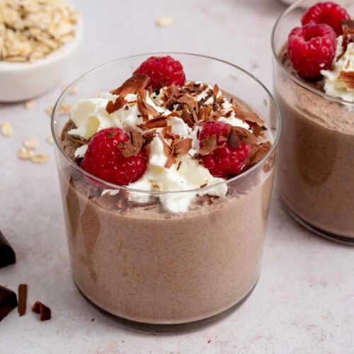 A jar of blended chocolate overnight oats with raspberries, whipped cream, and chocolate shavings.