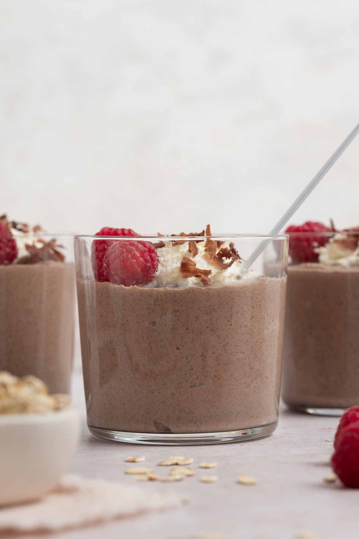 A profile view of a jar of blended chocolate overnight oats topped with whipped cream, shaved chocolate, and raspberries.