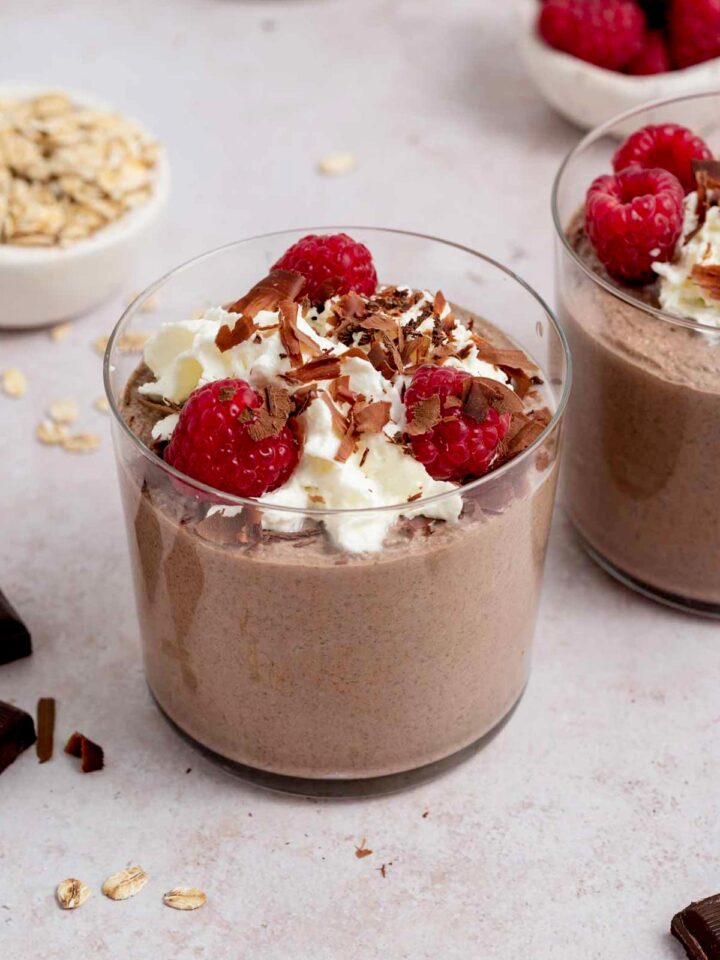 A jar of blended chocolate overnight oats with raspberries, whipped cream, and chocolate shavings.