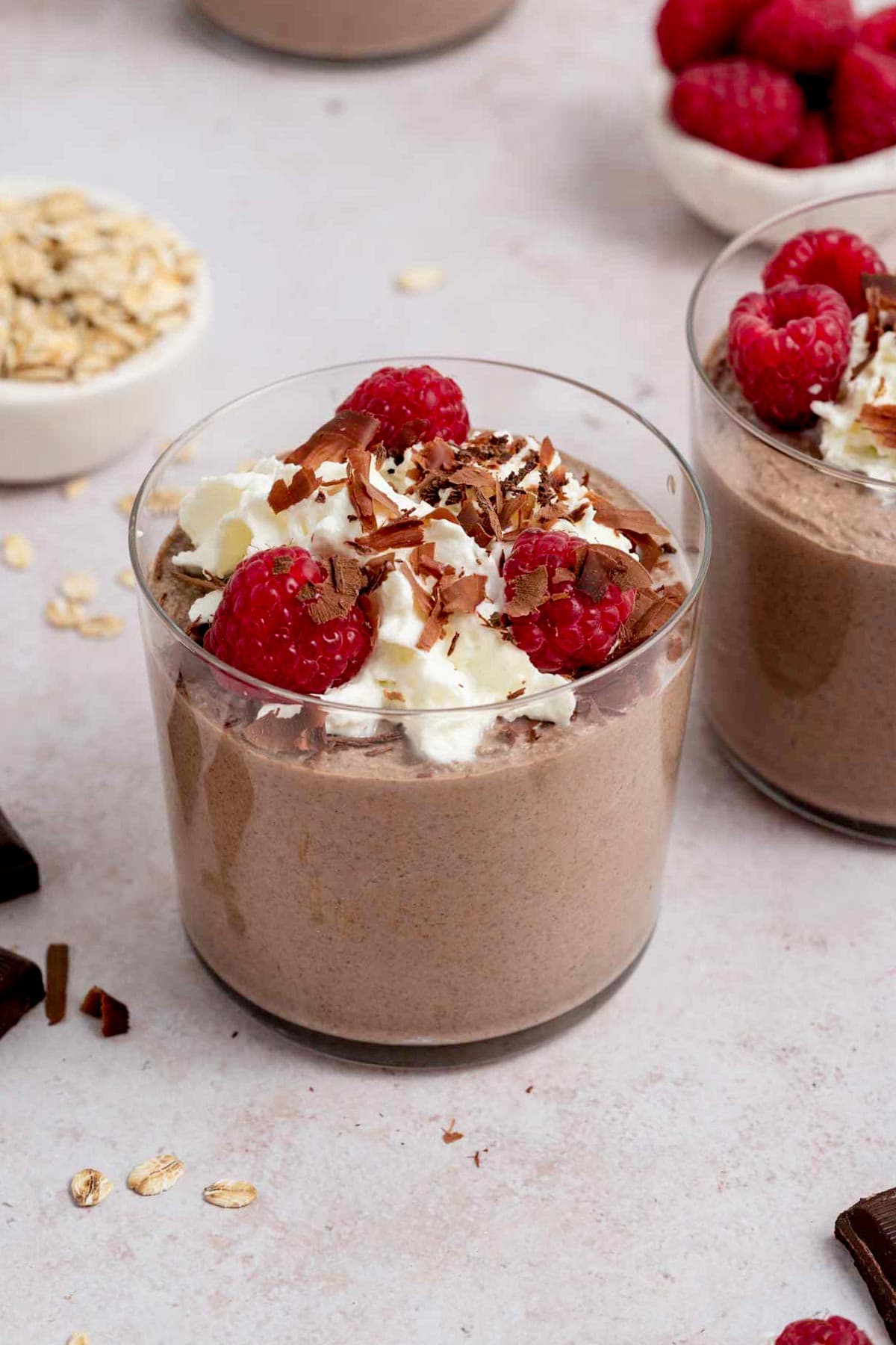 A jar of blended chocolate overnight oats with raspberries, whipped cream, and chocolate shavings.
