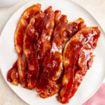 A plate of brown sugar bacon. A pink linen napkin on the side and a latte.