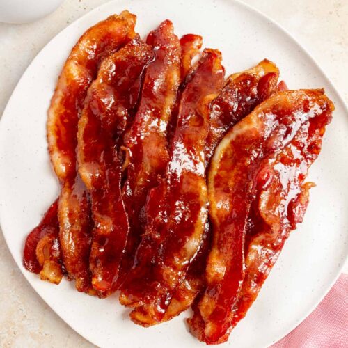 A plate of brown sugar bacon. A pink linen napkin on the side and a latte.