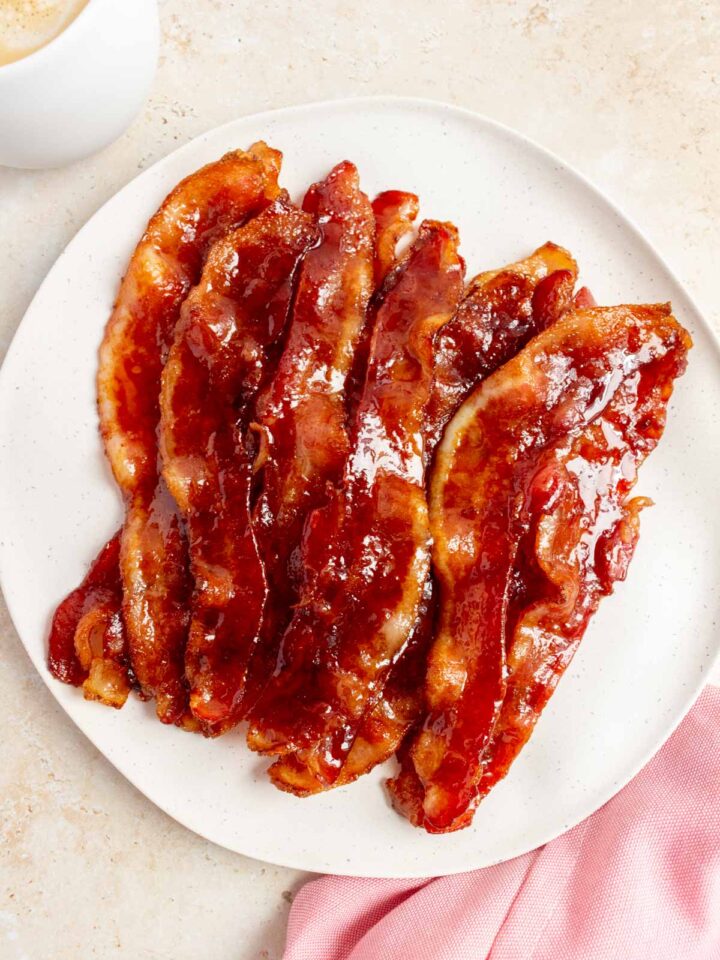 A plate of brown sugar bacon. A pink linen napkin on the side and a latte.