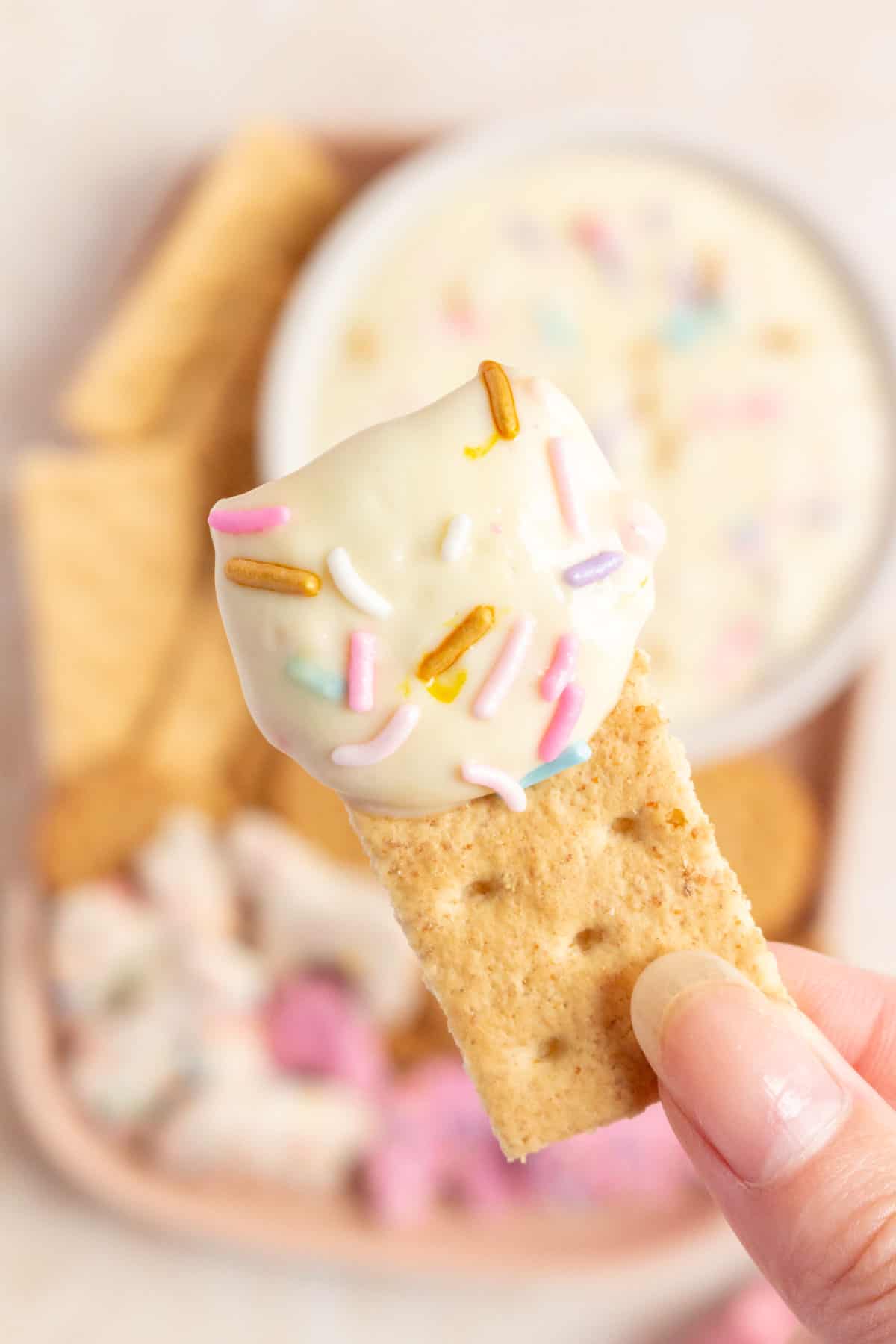 A graham cracker held up with funfetti greek yogurt dip on it.