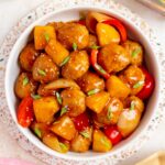Overhead view of a platter of sweet and sour meatballs topped with green onions and sesame seeds.